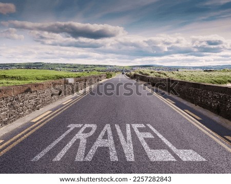 Small narrow high quality asphalt road with stone fences on each side and big sign travel. Blue cloudy sky and green fields. Warm sunny day. West of Ireland. Tourism concept.