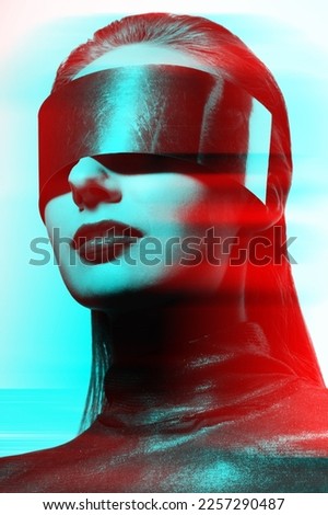 Woman studio portrait with big silver futuristic glasses or helmet covering her eyes in red and blue color split effect. Model wearing dark blouse in white studio background. Futuristic looking style