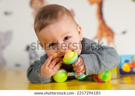 Cute baby boy nibbles and eats colourful toys because her small new teeth grow. Playground for babies Royalty-Free Stock Photo #2257296185