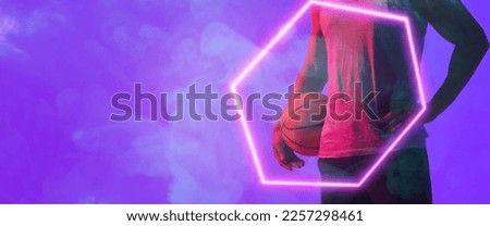 Midsection of biracial basketball player with ball standing by hexagon over smoky background. Blue, composite, copy space, hand, sport, competition, illustration, illuminated, shape and abstract.