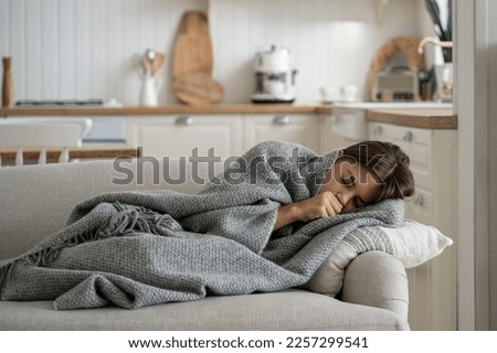 Sick girl child covered with blanket lying on sofa at home coughing, having flu symptoms. Ill kid with fever wrapped with plaid having chills shivering. Children and respiratory viruses Royalty-Free Stock Photo #2257299541