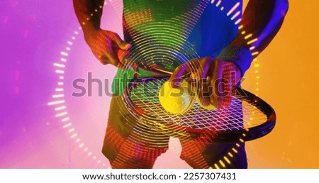 Midsection of african american male tennis player with racket and ball over circular pattern. Copy space, composite, sport, competition, neon, hand, illuminated, shape and abstract concept.
