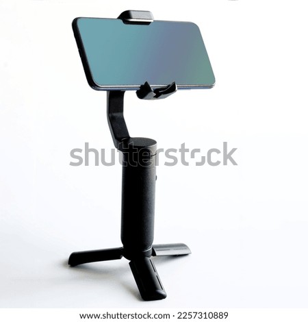 Modern stabilizer-gimbal for photo-video shooting and small tabletop tripod along with mobile phone on white background. Gadgets for blogging, streaming, video and photography. Copy space. Close-up Royalty-Free Stock Photo #2257310889