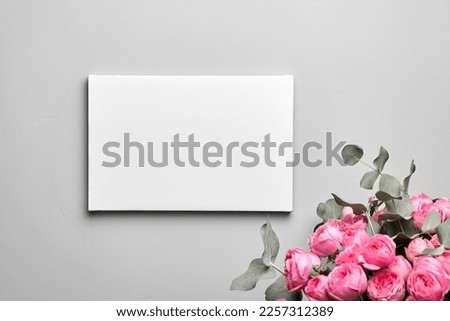 White canvas mockup hanging on grey wall and bouquet of pink roses with eucalyptus leaves. Empty blank canvas, interior decor
