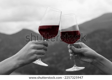 Friends clinking glasses of wine in mountains, closeup. Black and white photo with red accent