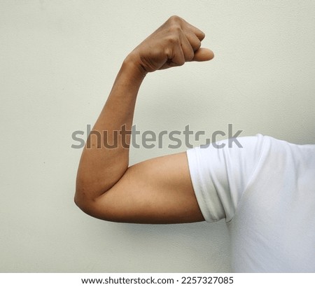 Close-up view of muscular asian woman in tanned white shirt raising arms at right angles  clenched fists to flex muscles  On a white background and the concept of exercise to stay healthy