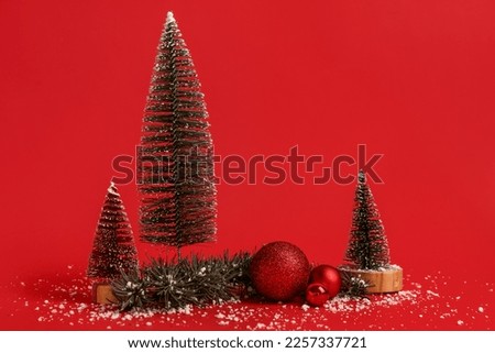 Composition with decorative Christmas trees, balls, coniferous branch and snow on red background