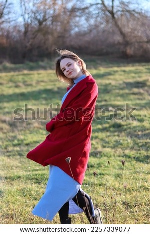 A girl in a red coat stands in nature.A woman walks.Pose in motion.Vintage retro photo.Beautiful image.A woman takes off her coat.Walks on green grass.Cold season.Lonely girl.
The emotion.Loneliness.