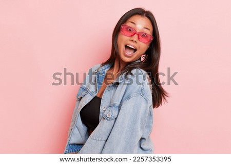 People lifestyle concept. Amazed Asian young woman with wide opened mouth poses half turned in jeans jacket and black top feels excited has shocked expression isolated over pink background.  Royalty-Free Stock Photo #2257353395