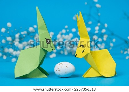 Two paper origami bunnies and an Easter egg on a blue background. Crafts with your own hands for Easter.