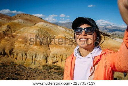 Cheerful woman tourist take a selfie with amazing mountain view. Happy young brunette enjoying vacation. Female traveller portrait.