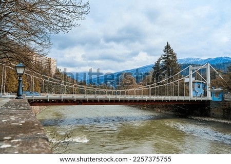 Landscape view of a suspension bridge over a mountain river in the Sakartvelo Mountains in early spring.