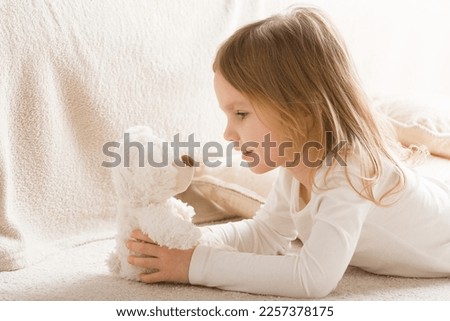 Adorable smiling little girl playing with white soft teddy bear on carpet at nursery room. Hands holding plush toy. Side view. Closeup. Royalty-Free Stock Photo #2257378175