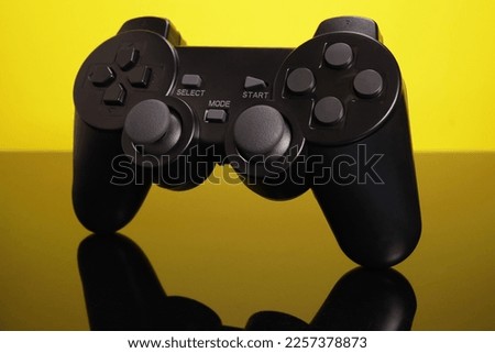 Wireless joystick gamepad controllers on mirror surface on yellow background, computer video game concept