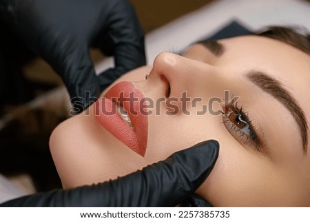 Finished work on permanent lip makeup for a model, lips close-up, the master tightens the corners of the lips with his fingers. Lip tattoo done Royalty-Free Stock Photo #2257385735