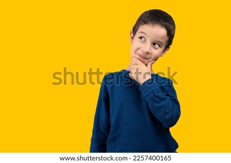Dark haired little child wearing winter sweater over isolated yellow background with hand on chin thinking about question, thoughtful expression.Pensive face. Concept of doubt and looking aside. Royalty-Free Stock Photo #2257400165