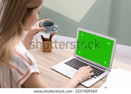 Young woman using laptop at wooden desk. Device display with chroma key