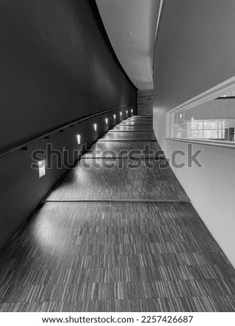 Black and white monochrome modern building interior curved narrow corridor hall with sloping floor and lamps on the wall