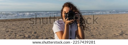 curly woman in white t-shirt taking photo on digital camera in Spain, banner