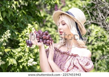 Photo of a young blonde woman in a hat, who is holding a bunch of grapes in her hand. Outdoor recreation,summer picnic.