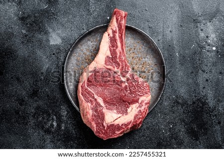Raw cowboy steak, rib eye steak with bone, beef marbled meat on butcher cutting board. Black background. Top view. Copy space.