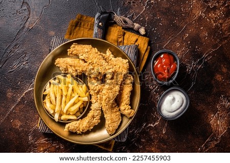 Dip fried Chicken breast strips with French Fries and sauces. Dark background. Top view. Royalty-Free Stock Photo #2257455903