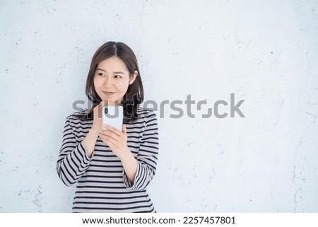 A smiling woman in her thirties who operates a smartphone in a bright living room.