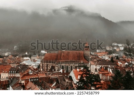 Panoramic view of Brasov old town from White tower. Cityscape with Black church, historical buildings tiled rooftops and Tampa mountain with Brasov sign in clouds. Winter city skyline from watchtower.