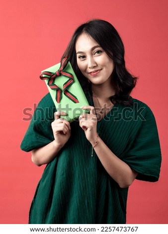 A studio portrait of a young beautiful Indonesian Asian woman in a casual green shirt looks happy as she is holding a gift. isolated on white background.