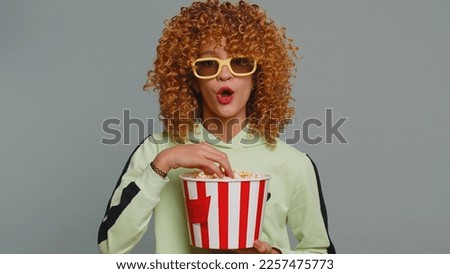 Excited young teenager school girl in 3D glasses eating popcorn, watching interesting tv serial, sport game, film, online social media movie content. Curly haired child kid on studio gray background