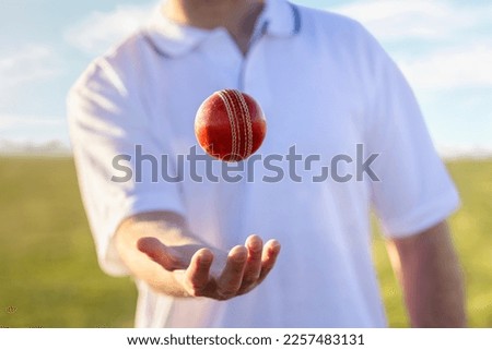Cricket player bowler throwing up and catching red leather cricket ball ready to bowl at cricket pitch