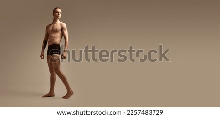 Full-length portrait of young man with fit, strong, muscular body posing in black boxers on studio background. Concept of men's health and beauty, body and skin care, fitness. Copy space for ad, text Royalty-Free Stock Photo #2257483729
