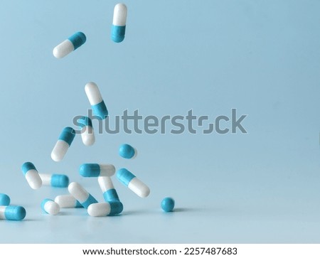 Falling blue medicine pill capsules on blue background. Antibiotics Royalty-Free Stock Photo #2257487683