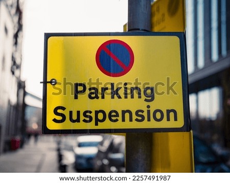 a bright yellow parking suspension sign by the road side attached to lamp post in the UK
