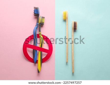 Plastic toothbrushes with prohibition sign and bamboo toothbrushes on pink blue background. Plastic free, eco concept