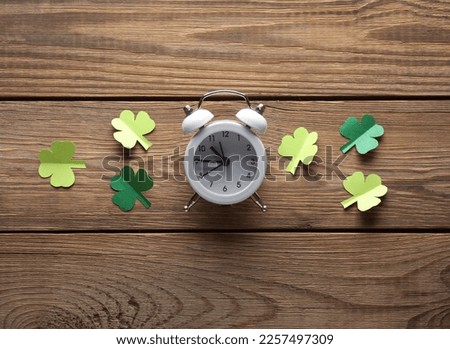Alarm clock with clover leaves on a wooden table. St.Patrick 's Day. Flat lay