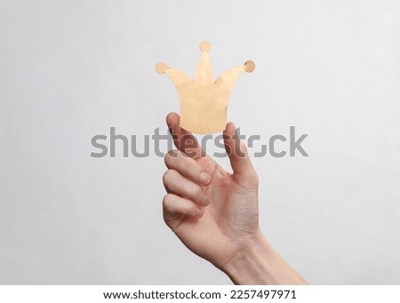 Hand holds paper cut golden crown on a white background