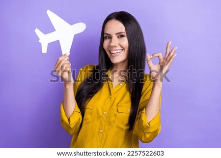 Photo of pretty positive girl toothy smile hand hold paper plane demonstrate okey symbol isolated on violet color background