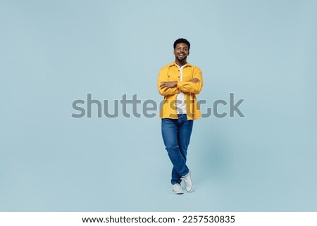 Full body young man of African American ethnicity 20s wear yellow shirt hold hands crossed folded look camera isolated on plain pastel light blue background studio portrait. People lifestyle concept Royalty-Free Stock Photo #2257530835