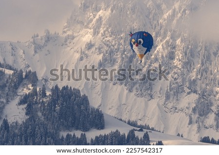Hot Air Balloon. One bird shape hot air ballooning flying against snow covered mountain in winter. 
