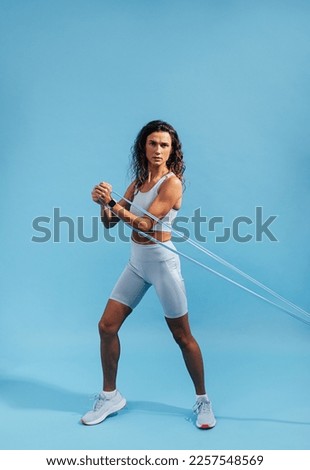 Slim muscular woman exercising with stretching band over blue background