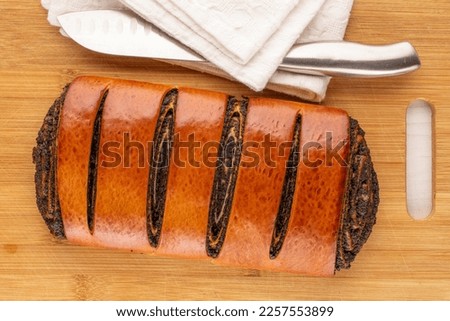 One appetizing poppy seed roll on bamboo board with white napkin and knife, macro, top view.