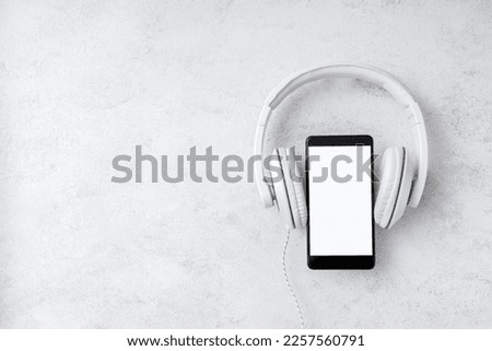 Top view of smartphone with blank bright screen and headphones on the desk. Empty space
