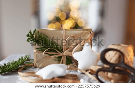 Christams present in golden wrapping paper, natural ribbon and tree with bokeh lights in background. Decoration and preparation for holidays.