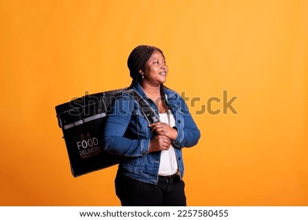Smiling restaurant courier standing in studio over yellow background carrying takeaway thermal backpack ready to deliver meal order to customer. Food transportation service and takeout concept