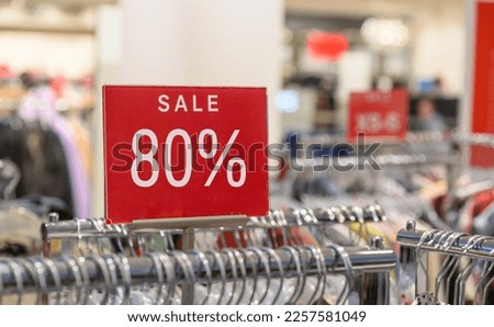 Red 80 % sale sign in store with clothes on hangers