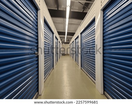 A long hallway with many blue doors inside of a storage locker facility. Royalty-Free Stock Photo #2257599681