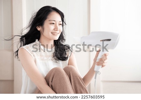 Asian woman with black hair using a hairdryer