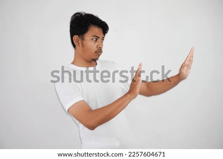 Displeased handsome young asian man wearing white t shirt showing stop sign isolated on white background