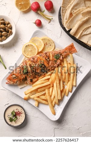 Tasty baked fish with rice on plate with french fries, lemon slices, sauce 
